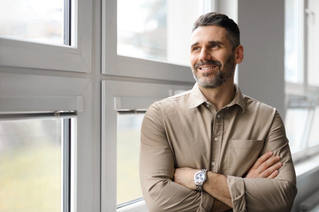Positive,Middle,Aged,Businessman,Standing,Near,Window,In,Company,Office,