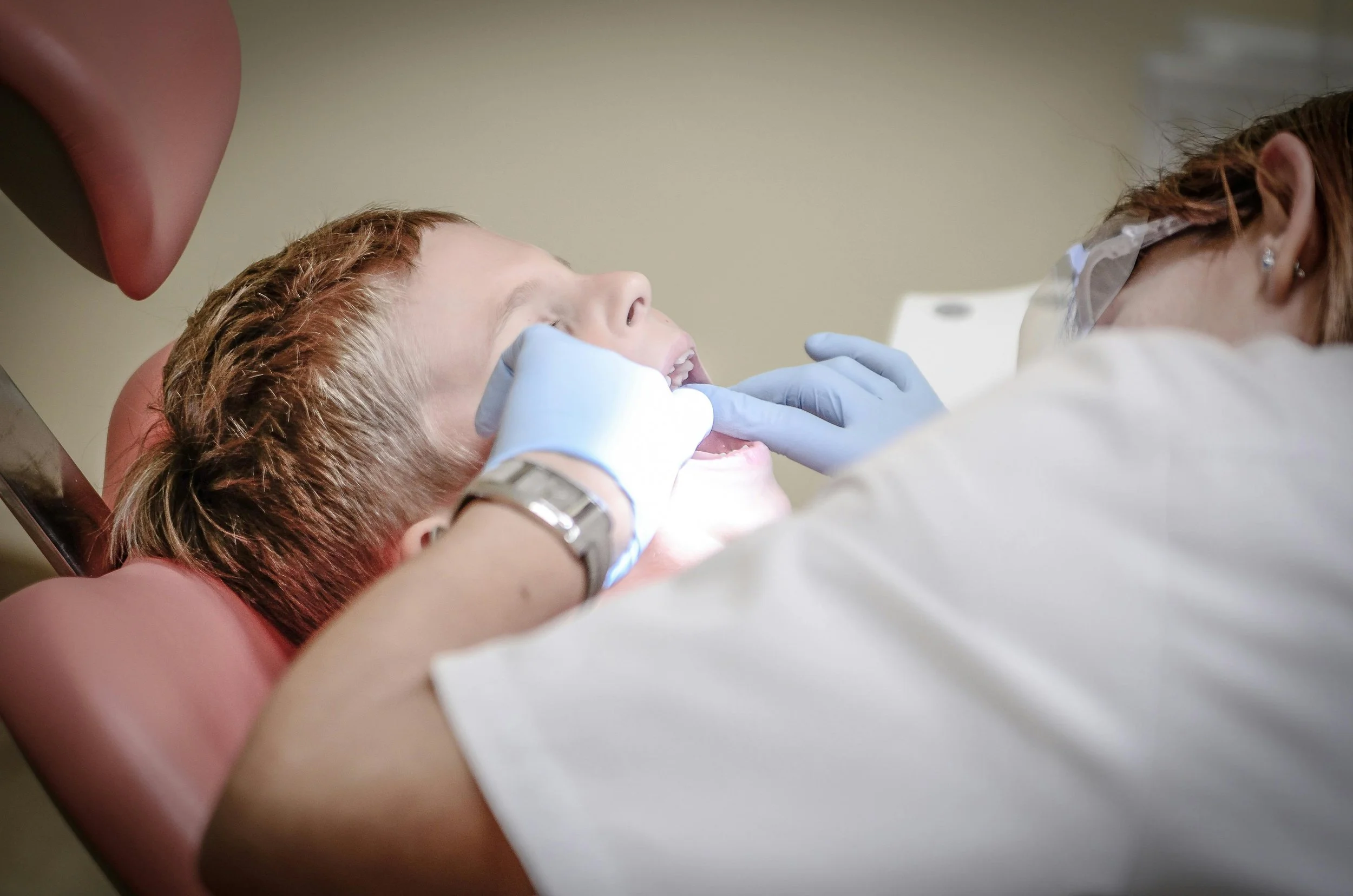 Child receiving a dental checkup from a dentist wearing gloves and protective glasses.