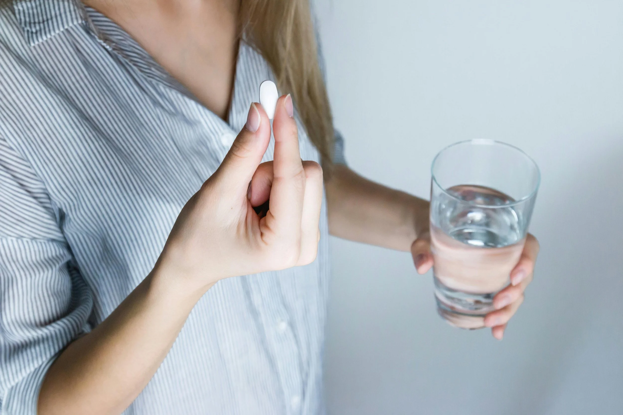 Person holding a pill and a glass of water, preparing to take medication for tooth pain or sensitivity.