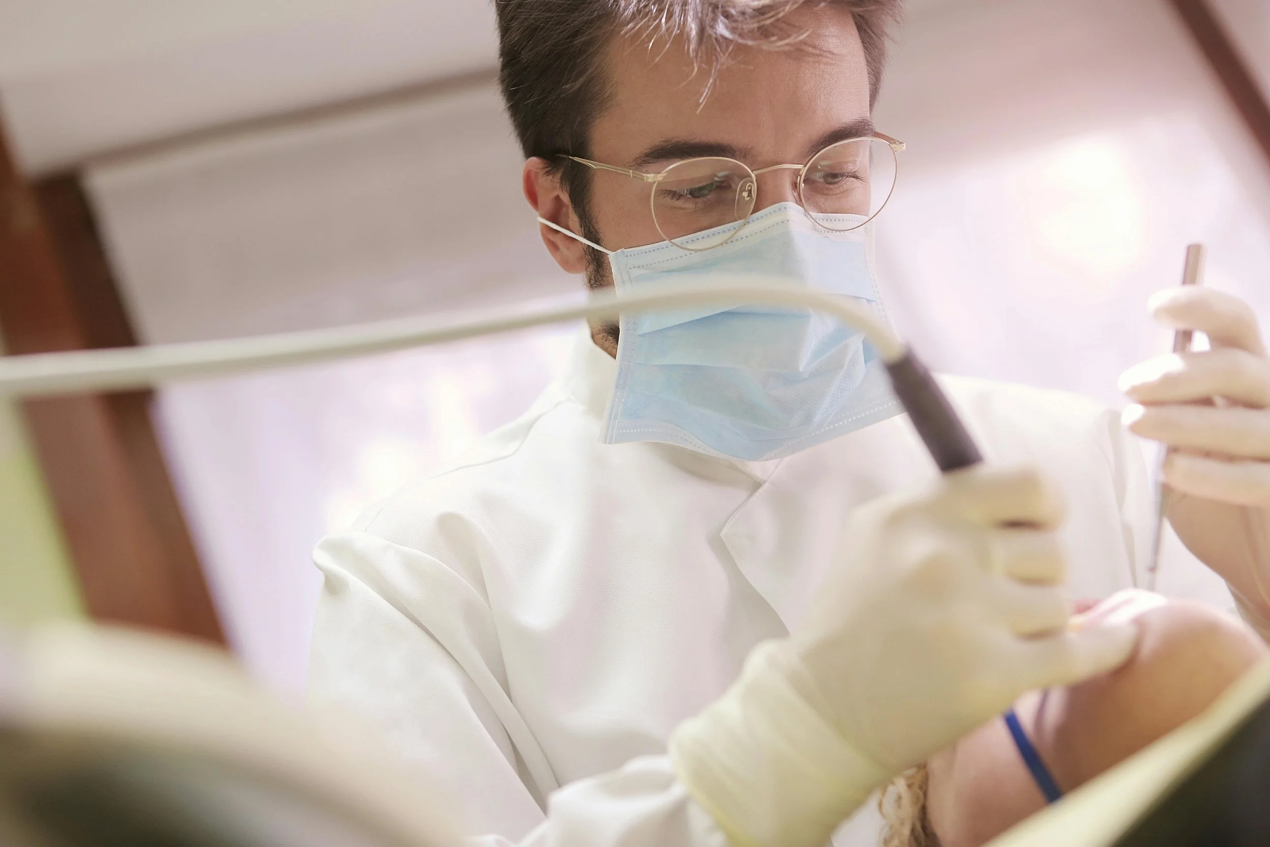 Dentist wearing protective mask and gloves performing a dental procedure on a patient.