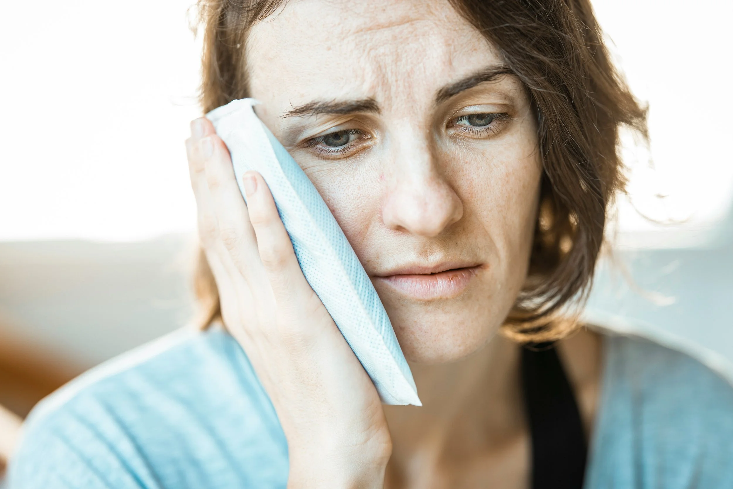Woman holding an ice pack to her cheek, appearing to be in discomfort or pain, possibly due to a dental issue or toothache.