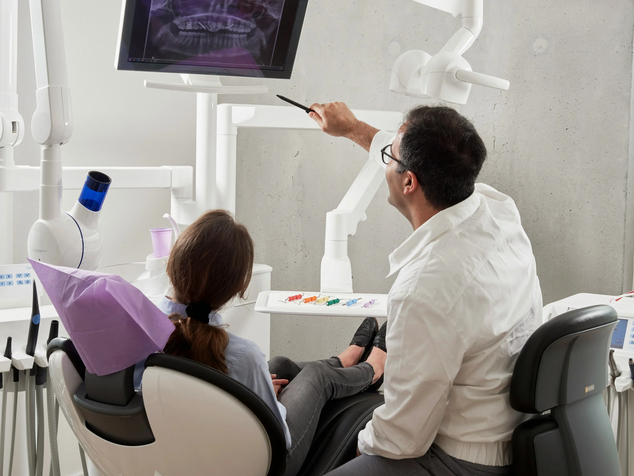 Dentist explaining a dental X-ray to a patient seated in a dental chair during a consultation in a modern dental clinic.