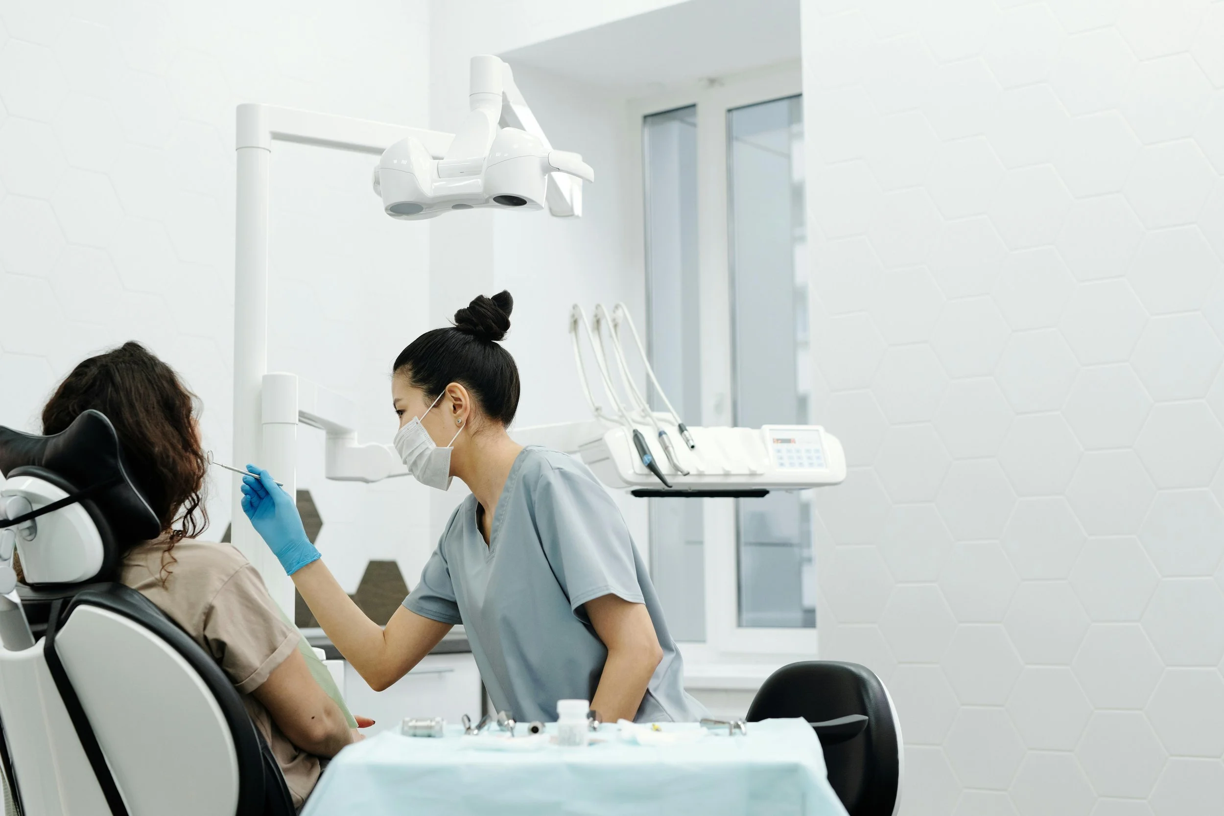 Female dentist wearing a mask and gloves examining a patient’s teeth in a modern dental clinic.