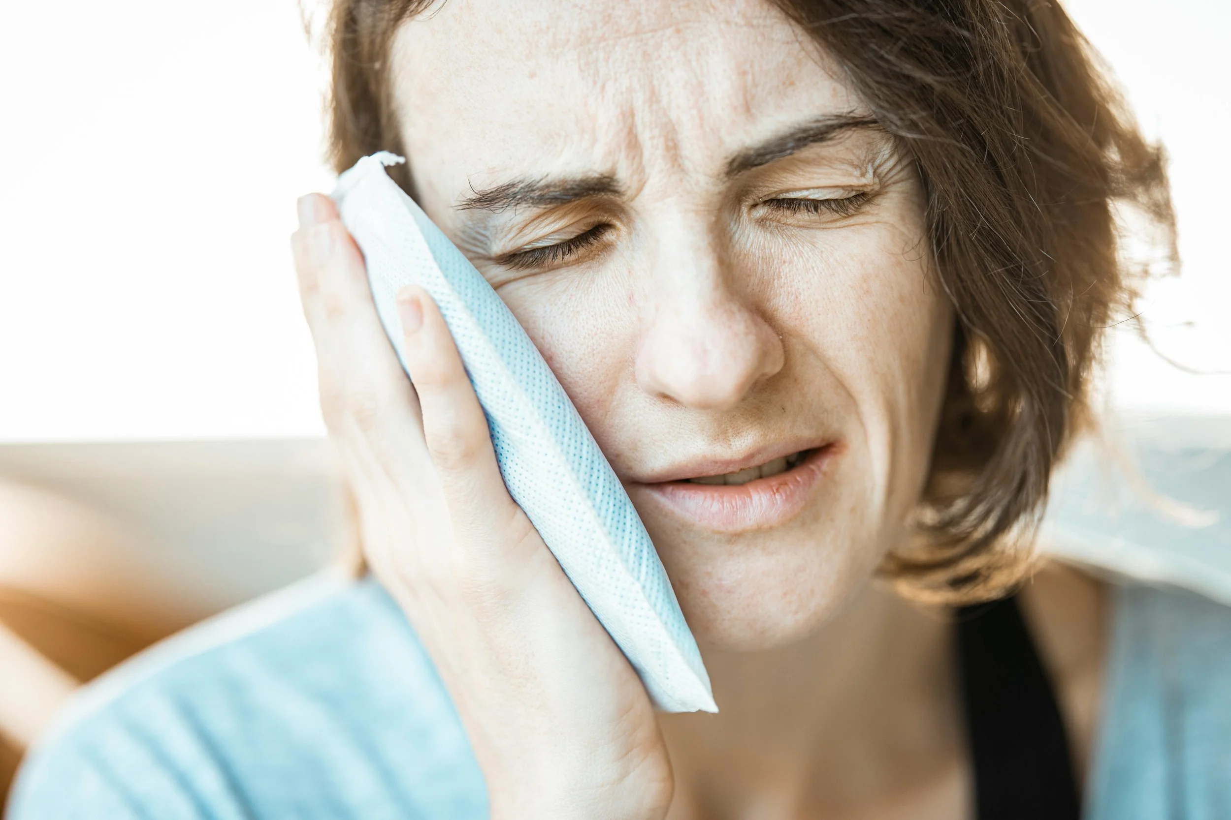 Woman holding an ice pack to her cheek, showing discomfort and pain, possibly due to a dental issue or toothache.