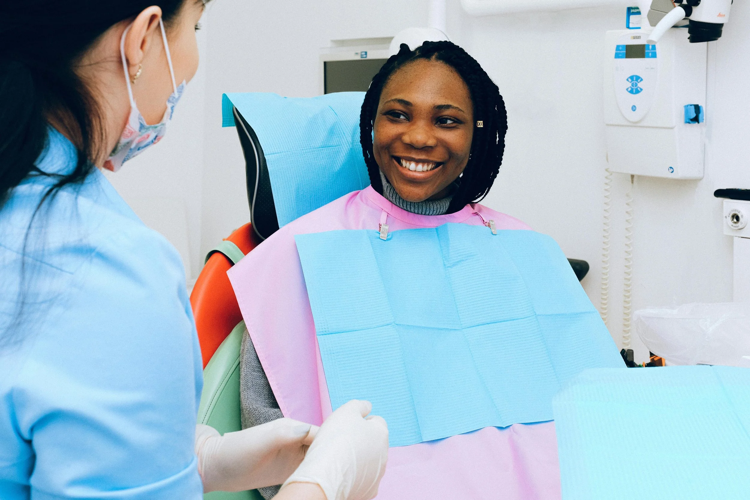 Smiling patient sitting in a dental chair while talking with a dentist during a checkup.